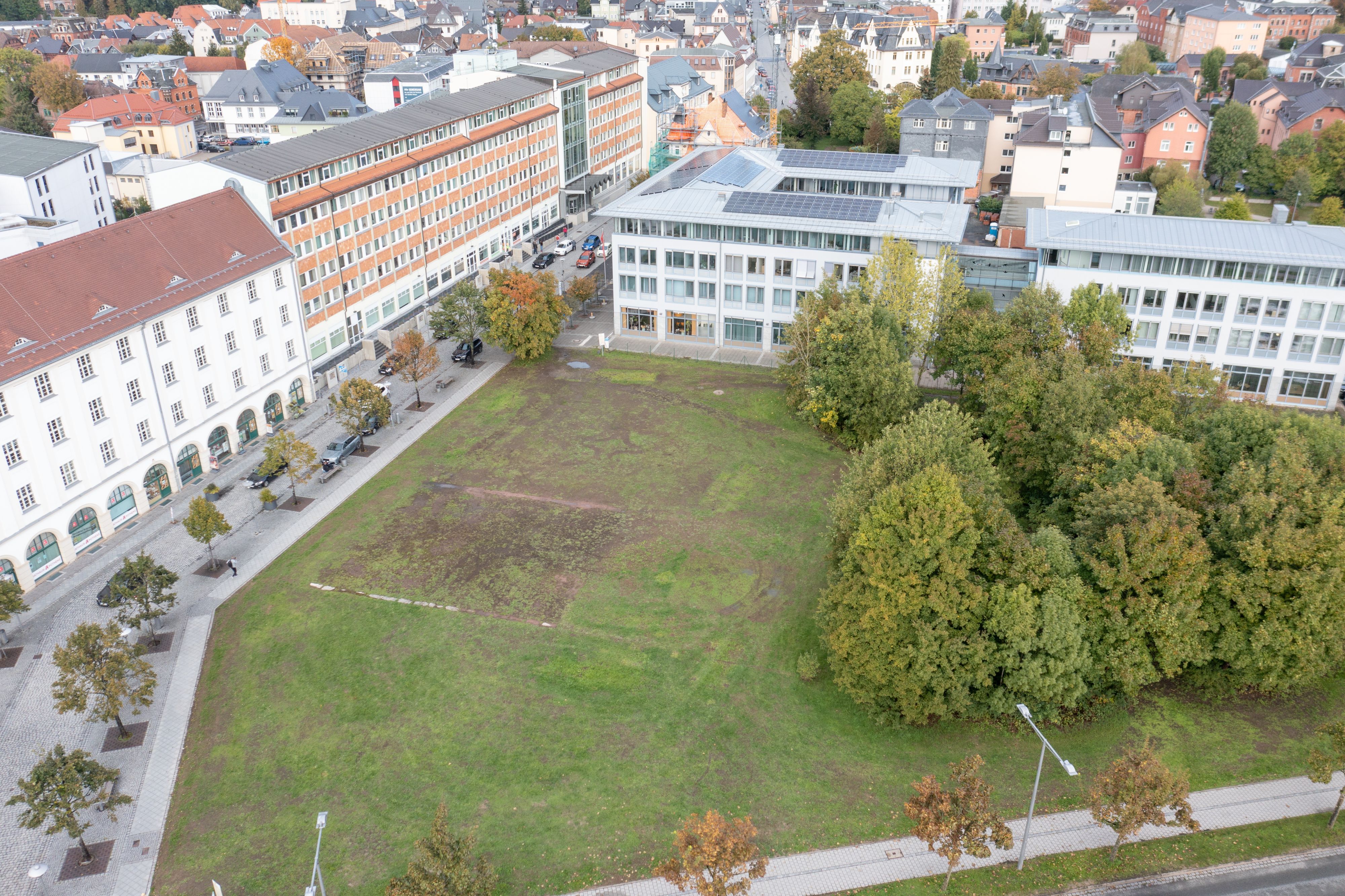 Drohnenaufnahme mit Blick auf das Woolworth-Gelände. Eine Fläche mit Wiese und Bäumen. Dahinter sind Häuser und Gebäude der Stadt zu sehen.