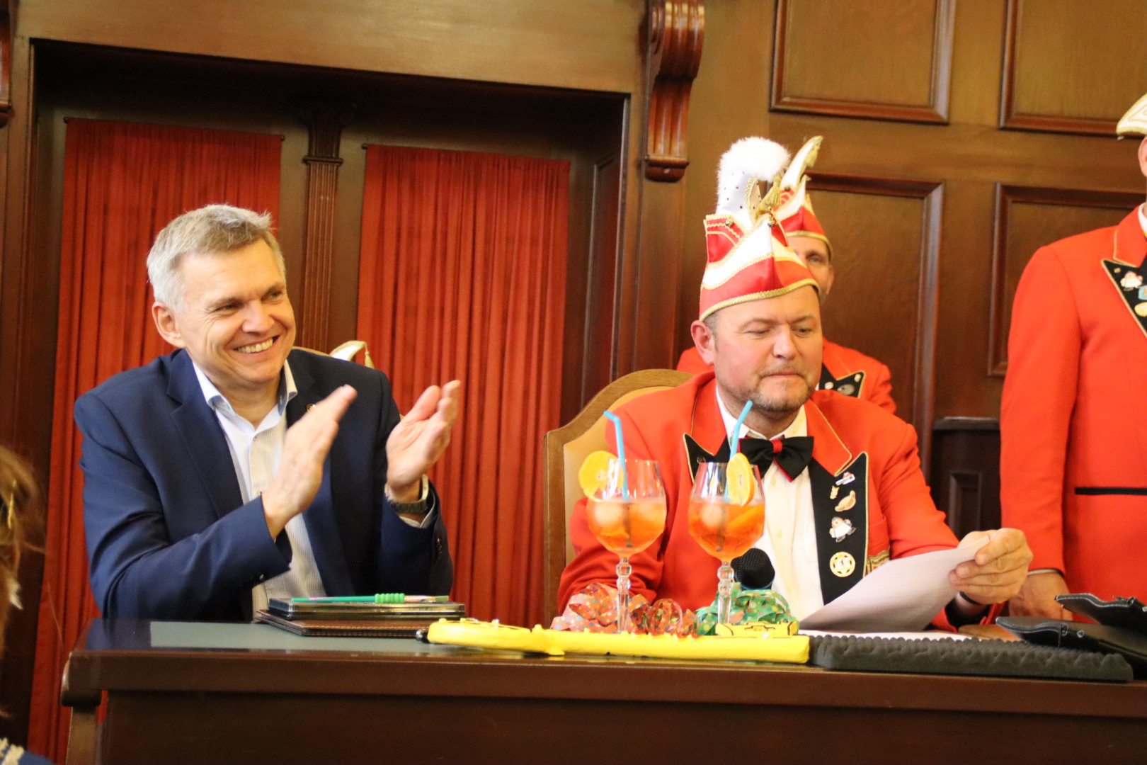 Der Bürgermeister sitzt neben dem Elferrat und klatscht in die Hände.