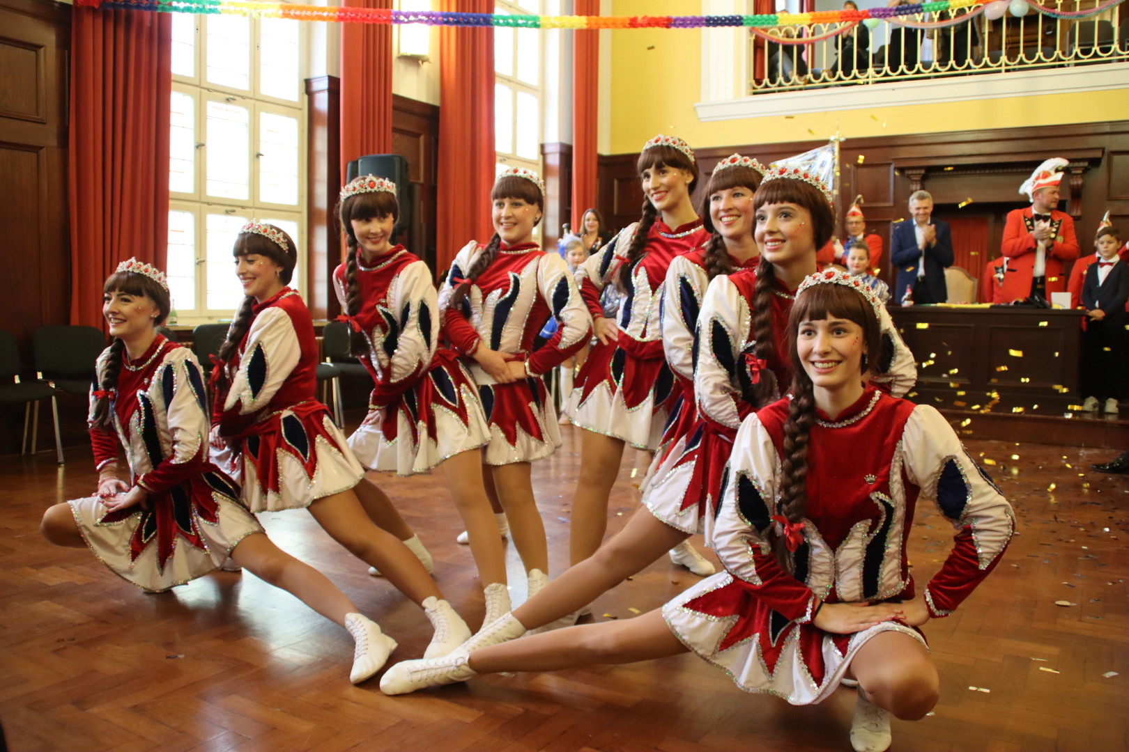 Eine Garde von Tanzmariechen in Tanzaufstellung. Im Hintergrund klatscht der Elferrad und der Bürgermeister.