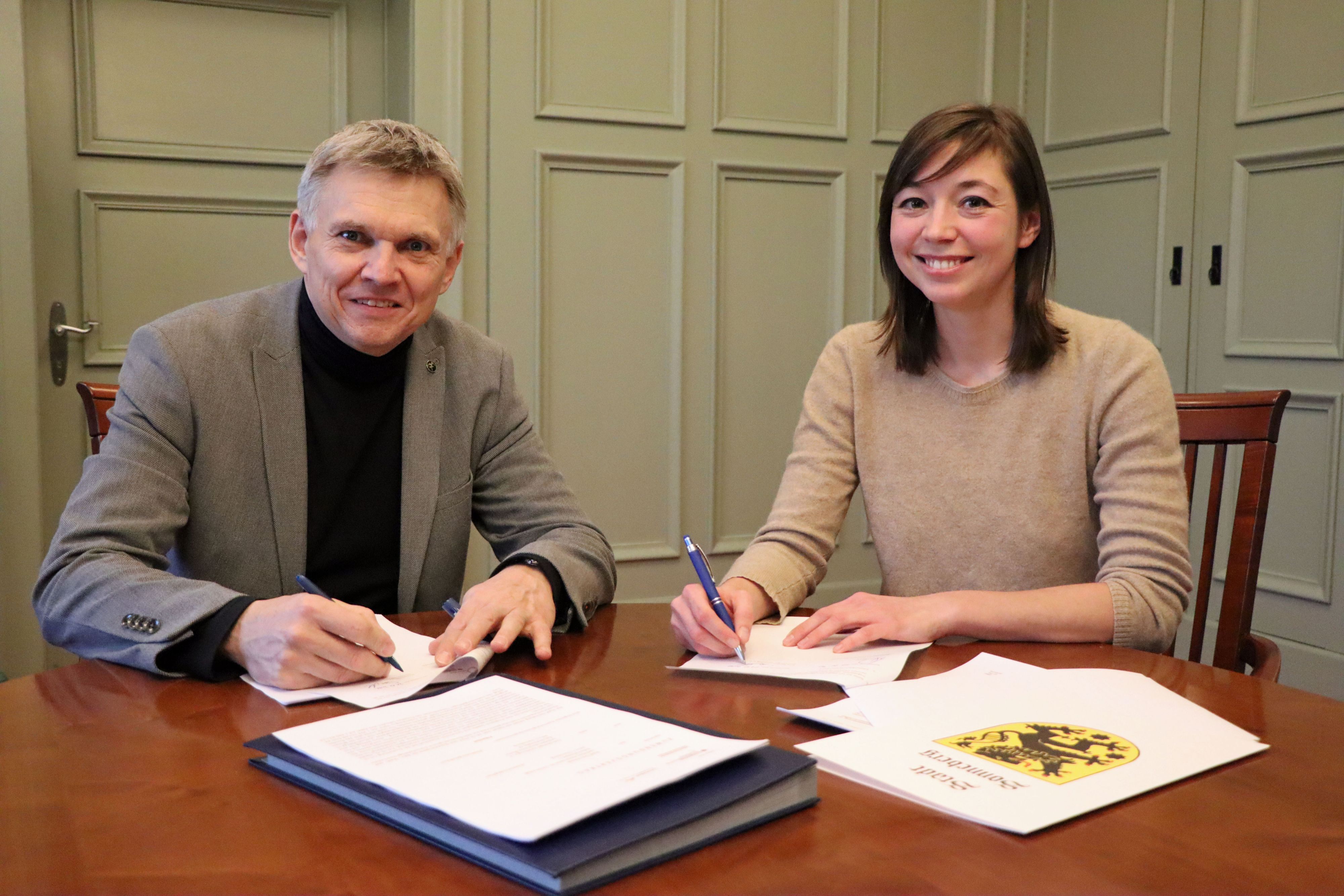 Ein Mann und eine Frau sitzen an einem Tisch und unterschreiben einen Vertrag.