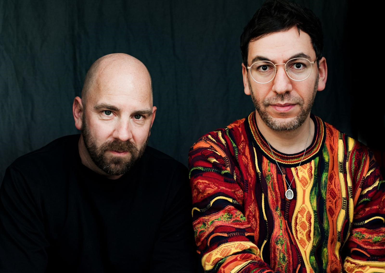 Ein schwarzgekleideter Mann und ein Mann mit buntem Strickpullover.