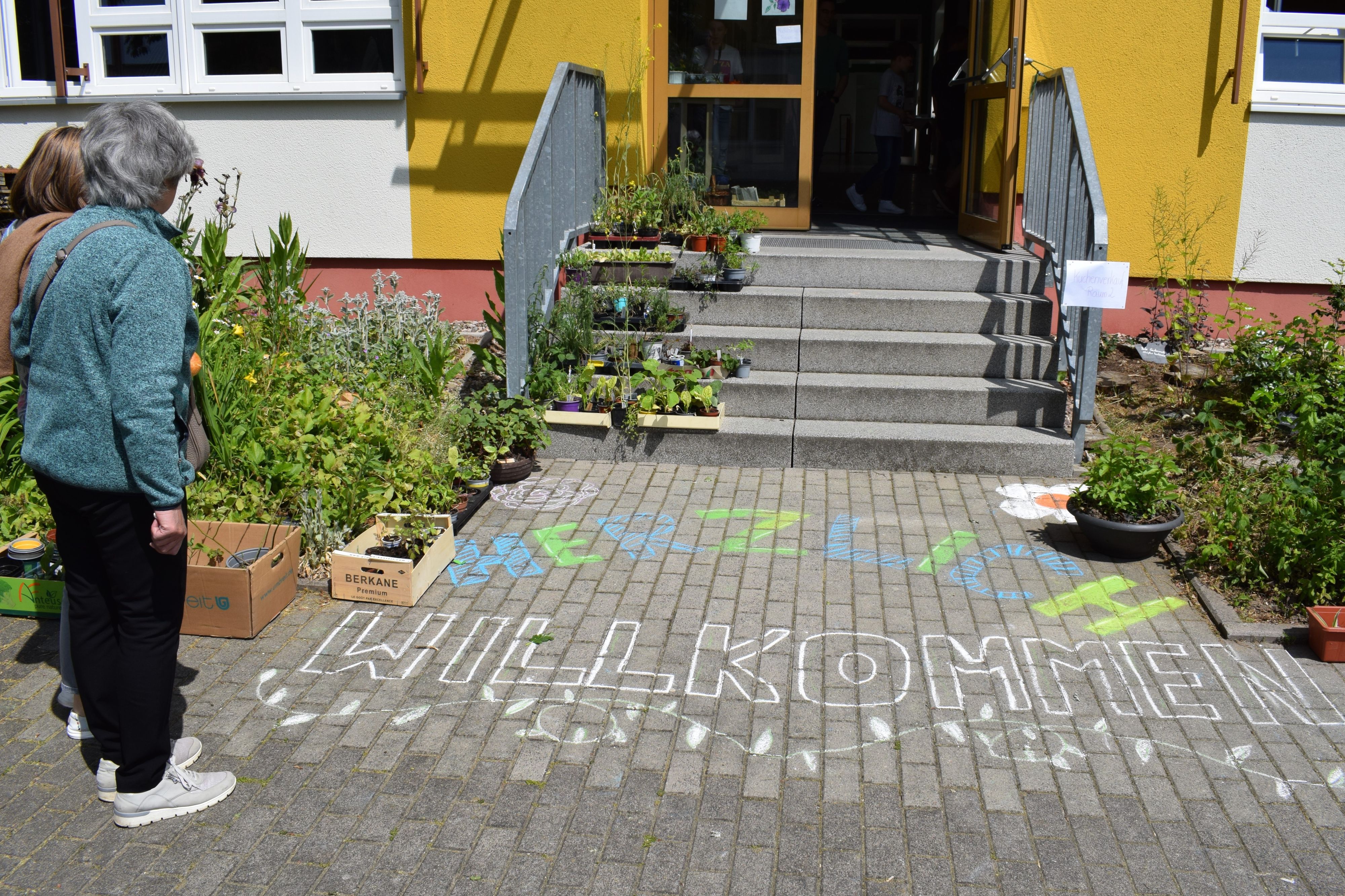 Auf dem Boden vor einer Eingangstür steht: Herzlich Willkommen.