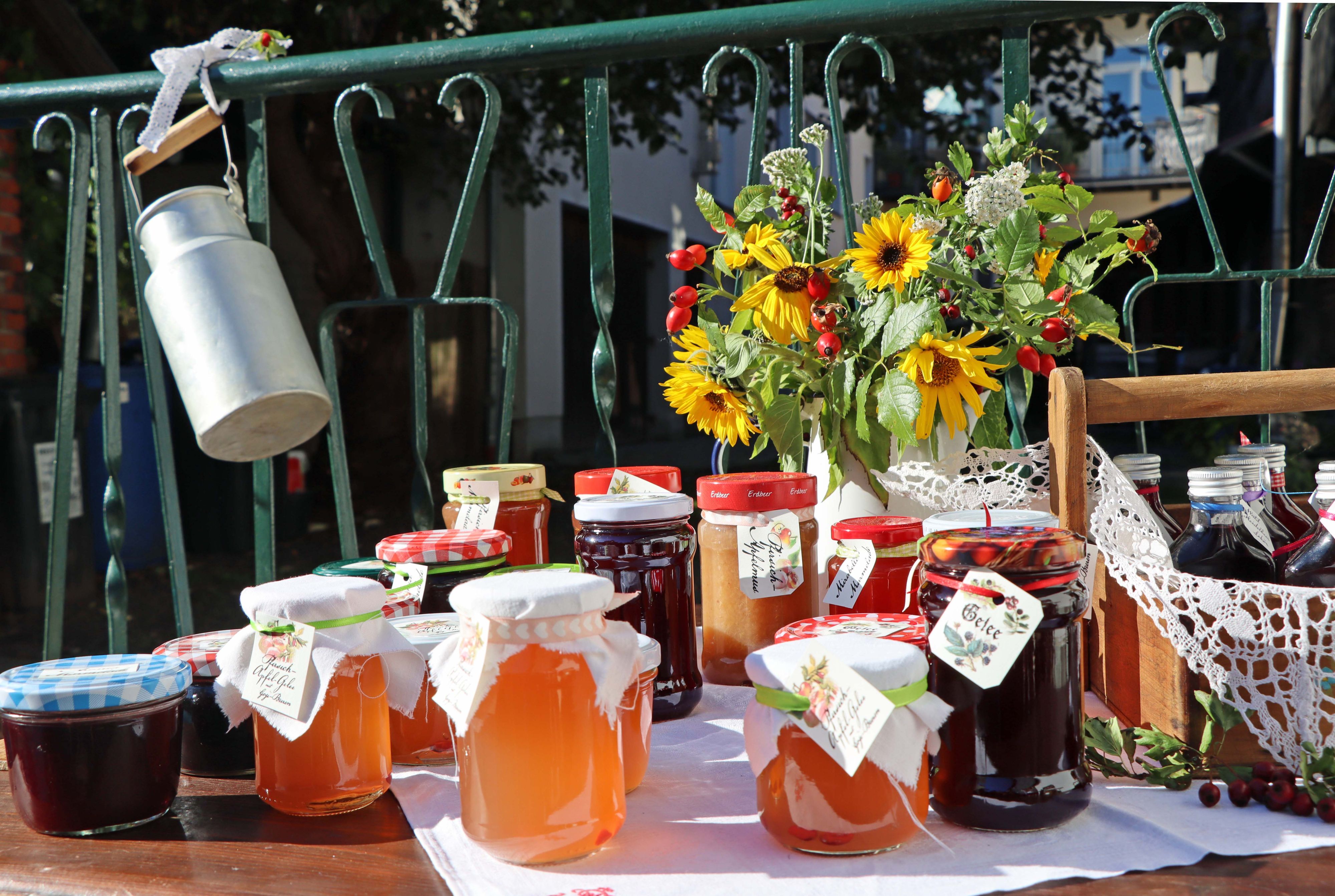 Auf einem Tisch steht selbstgemachter Gelee. Dahinter steht ein Strauß Sonnenblumen.