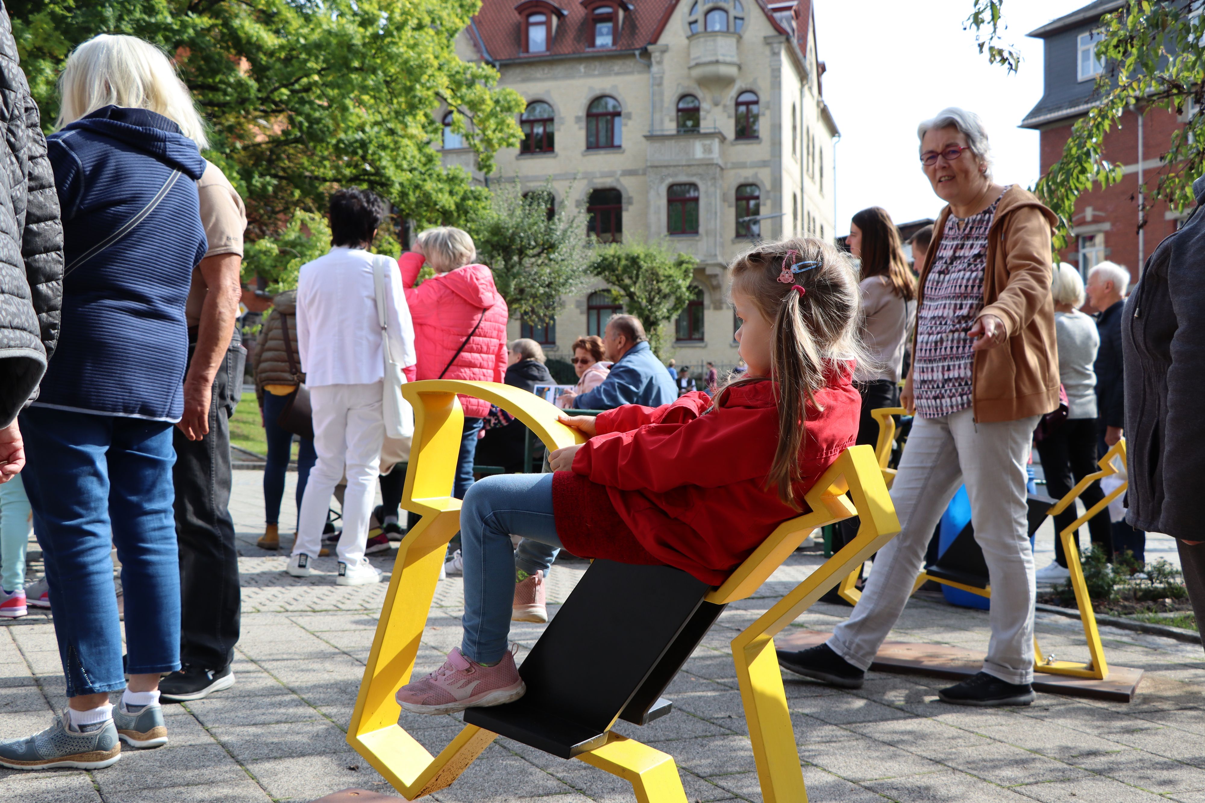Ein kleines Mädchen sitzt auf einer gelben Pferdekonstuktion aus Metall. Es ist das Pferd des Sonneberger Reiterleins. Im Hintergrund stehen viele Menschen.