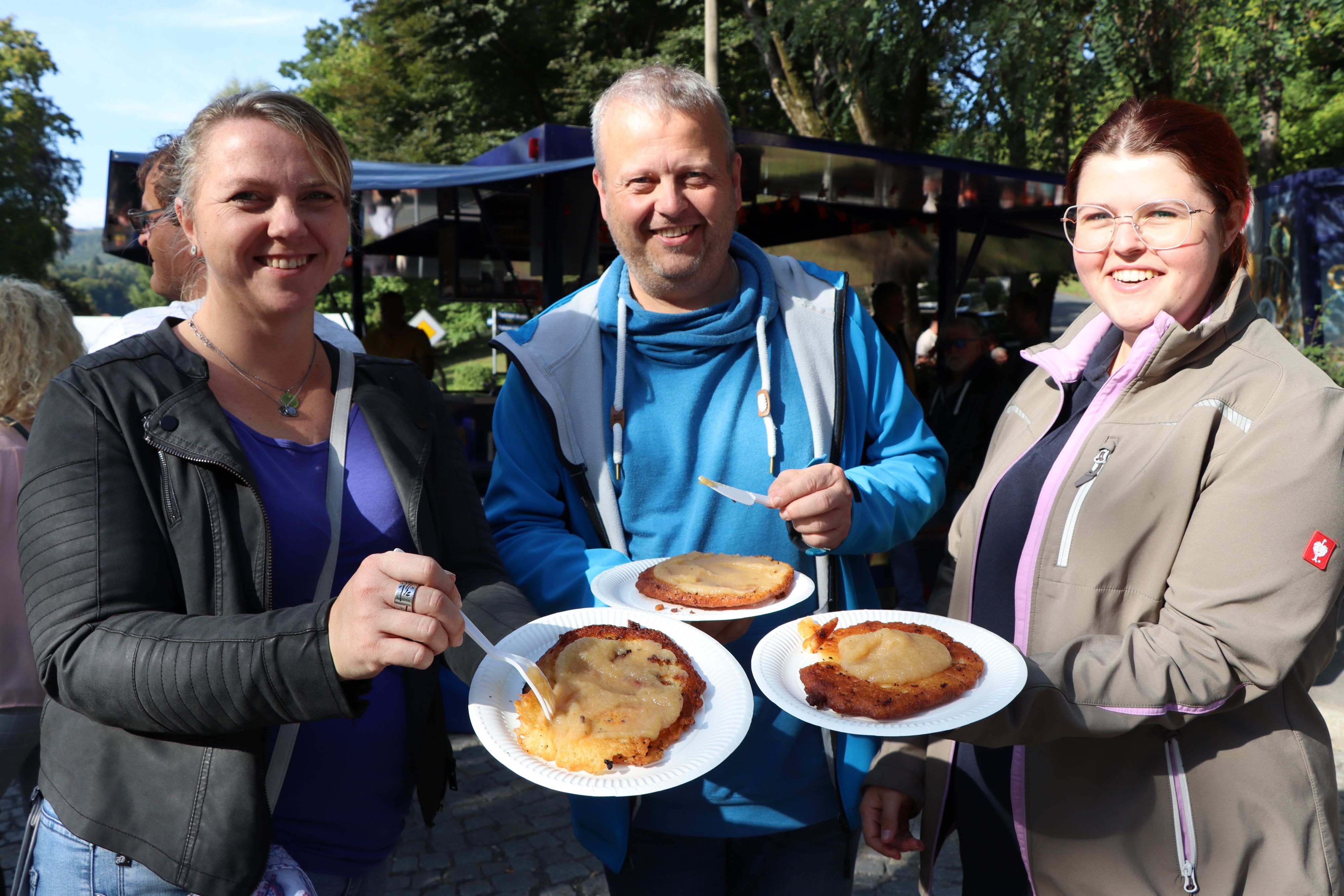 Drei Personen halten einen Pappteller in den Händen. Auf den Tellern ist Kartoffelpuffer mit Apfelmus.
