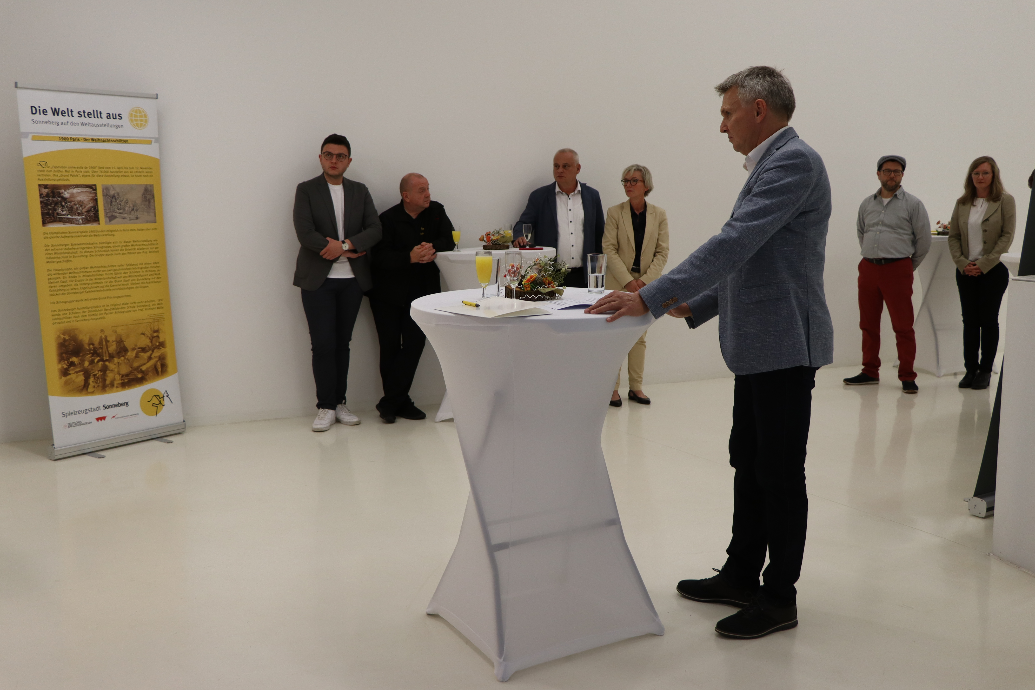 Ein Mann steht an einem Stehtisch und hält eine Ansprache.