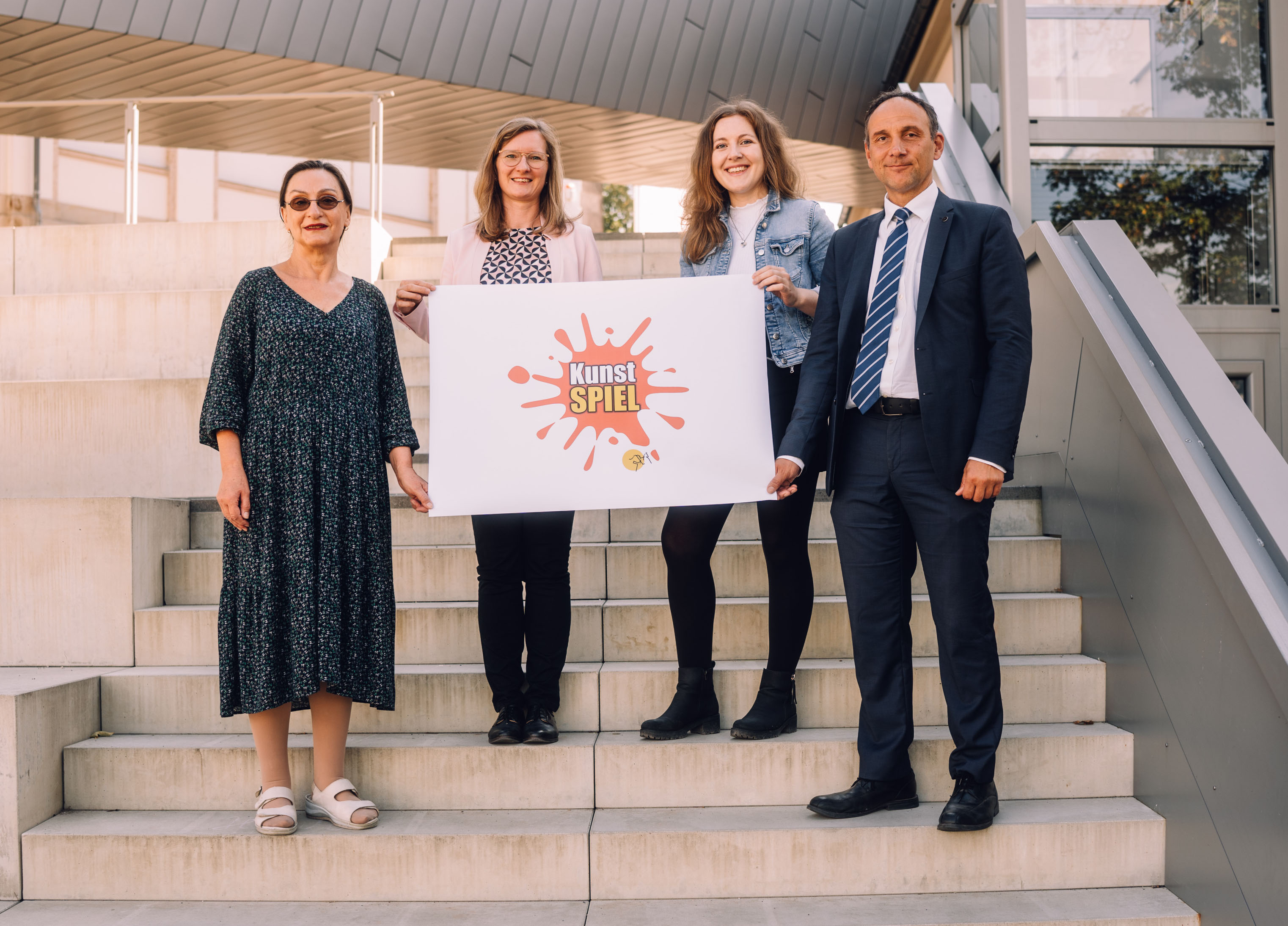 Vier Personen halten ein Plakat mit der Aufschrift Kunstspiel.