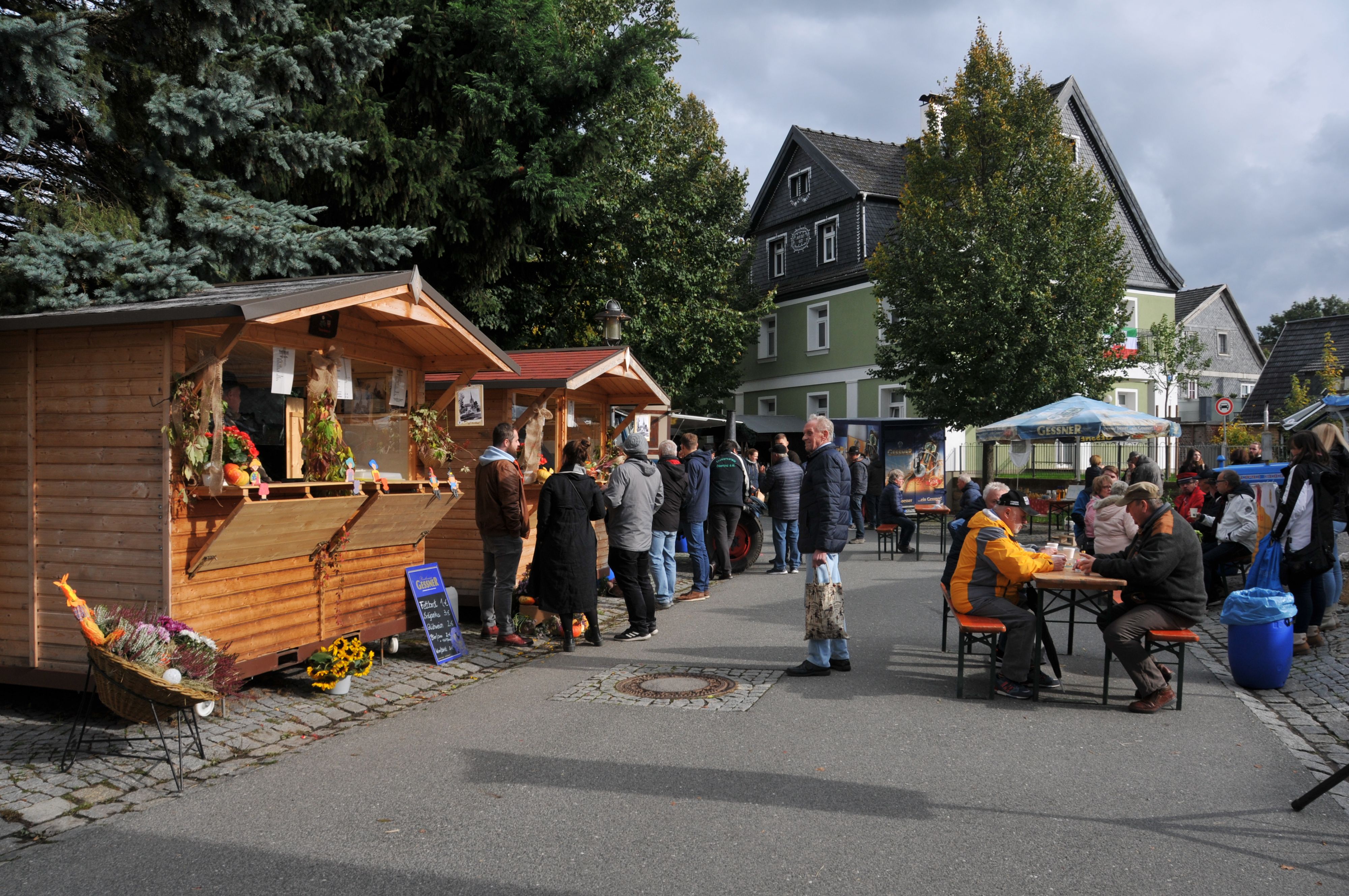 An einer Straße stehen verschiedene Verkaufshütten. Davor stehen Menschen.