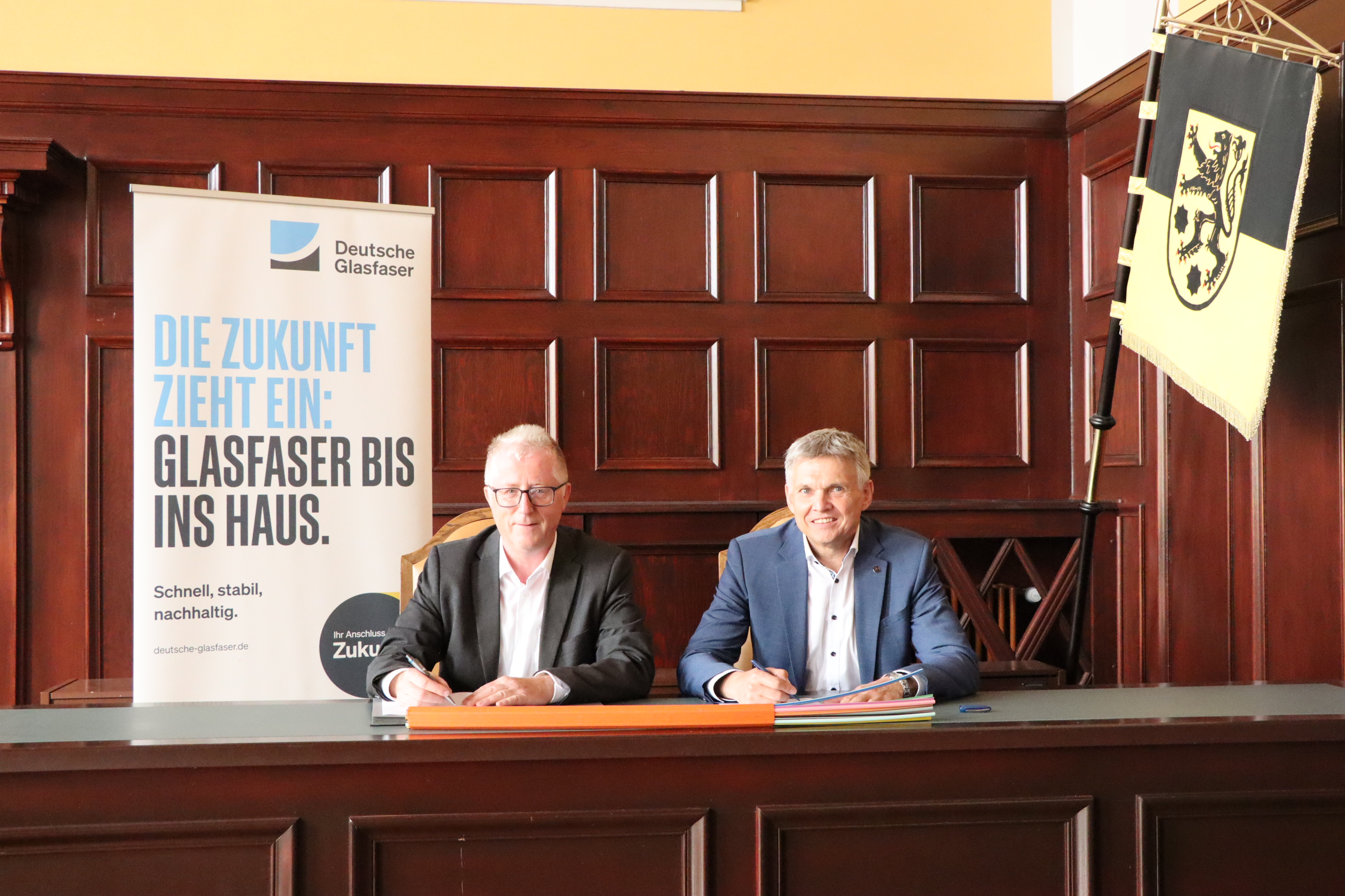 Zwei Männer sitzen an einem Tisch und unterschreiben einen Vertrag.