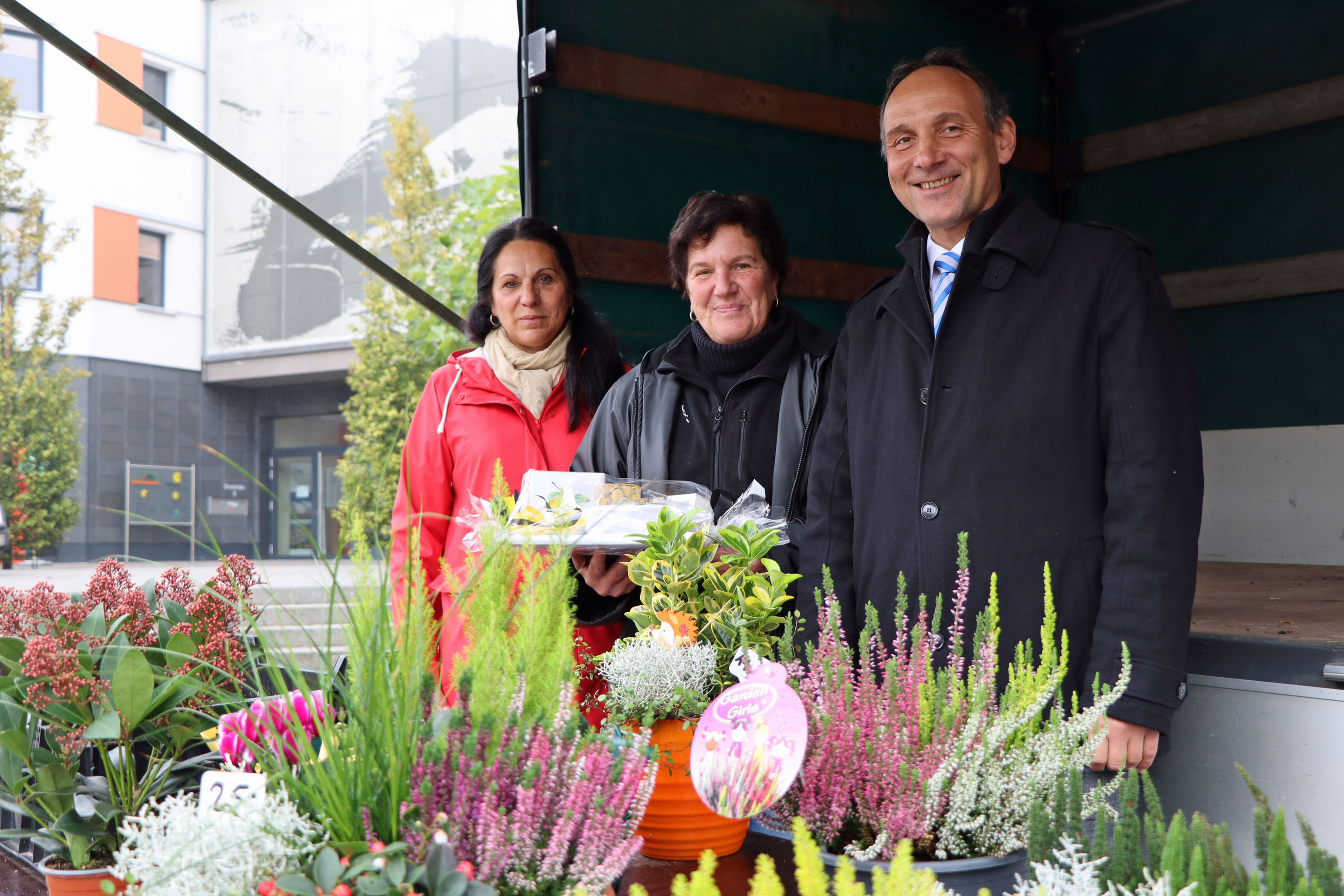 Zwei Frauen und ein Mann stehen hinter einem Tisch mit Herbstpflanzen.