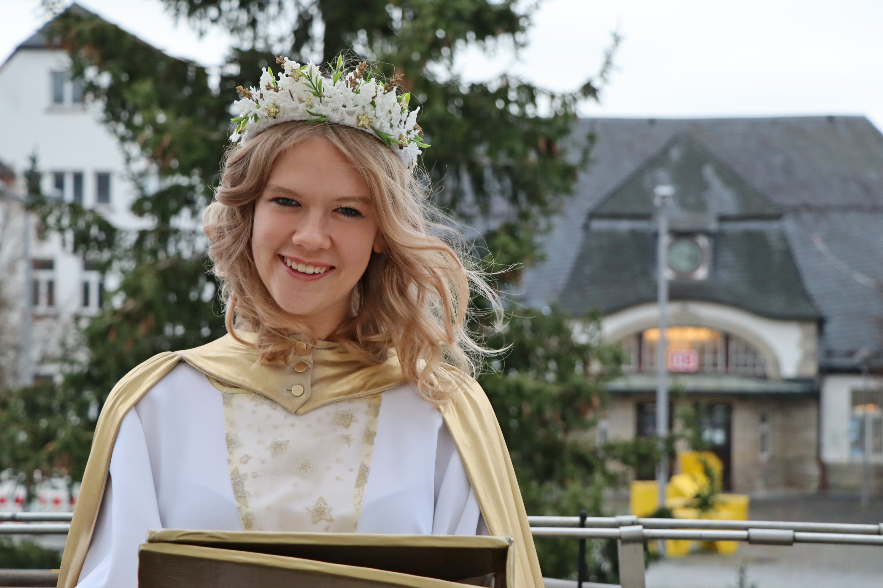 Eine Frau ist als Christkind gekleidet. Im Hintergrund ist der Bahnhof der Stadt Sonneberg.