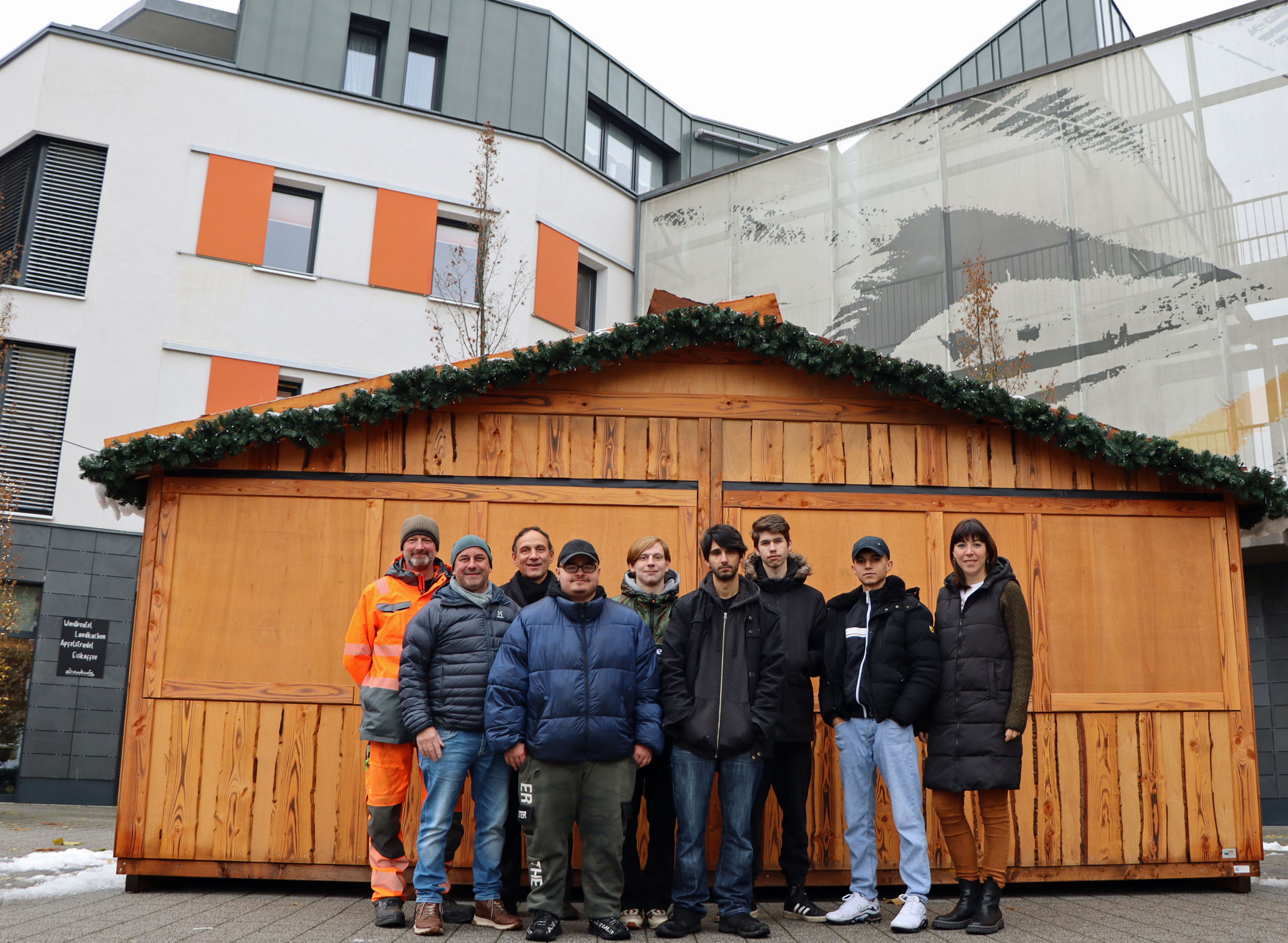 Mehrere Personen stehen vor einer großen Weihnachtsmarkthütte aus Holz.