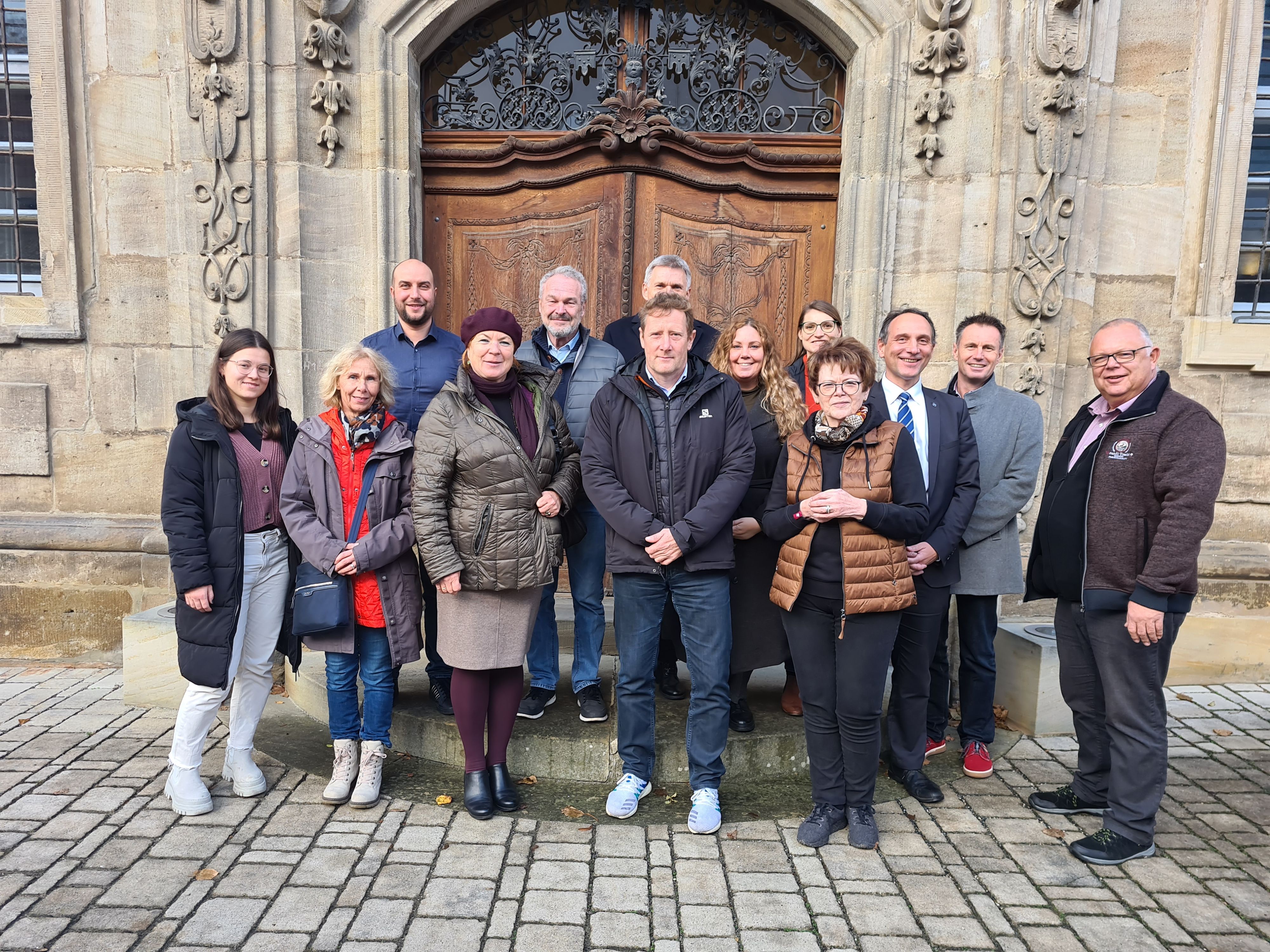 Eine Gruppe von Männern und Frauen steht vor dem Eingang eines Klosters.