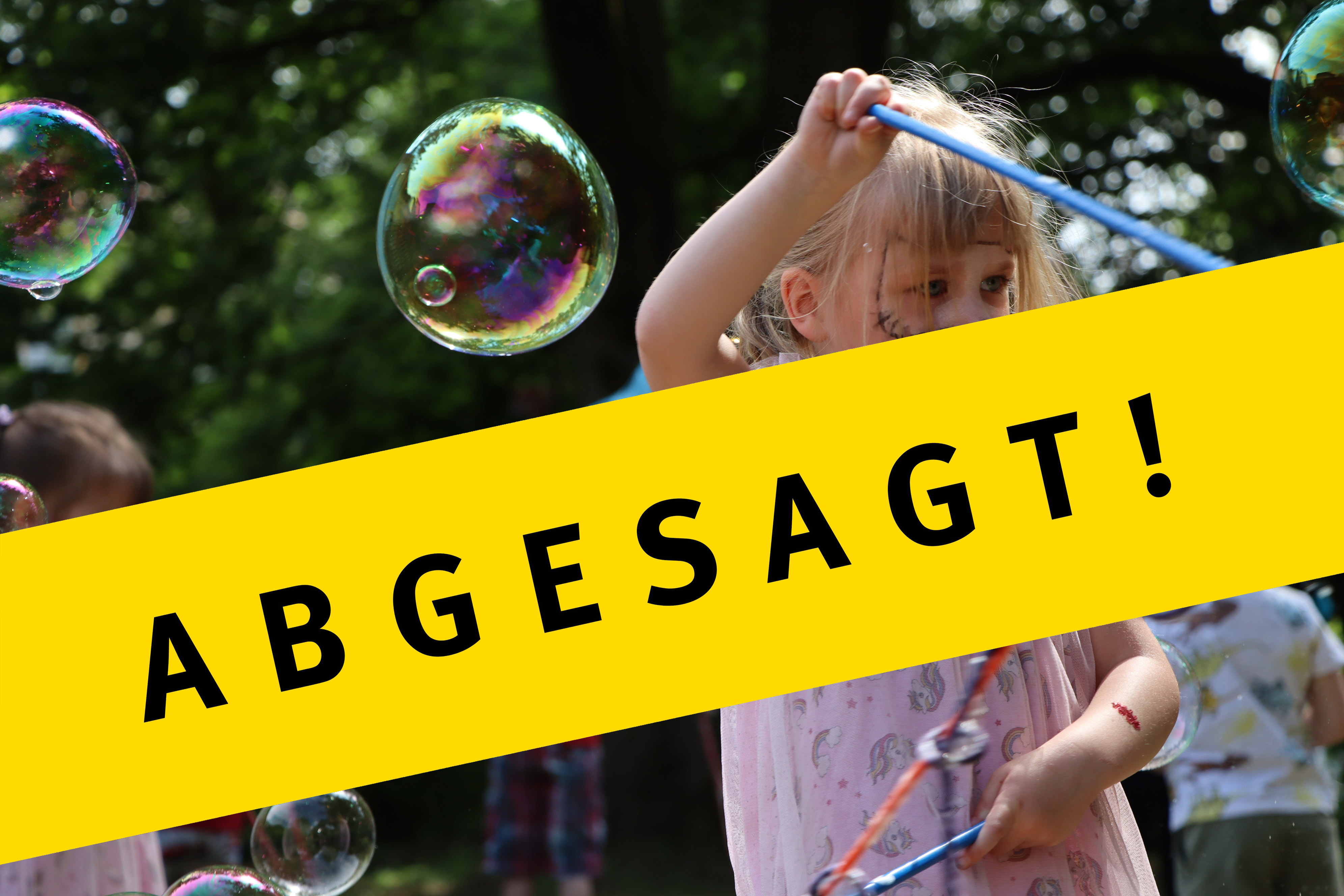 Im Hintergrund macht ein Kind Seifenblasen. Davor steht abgesagt.