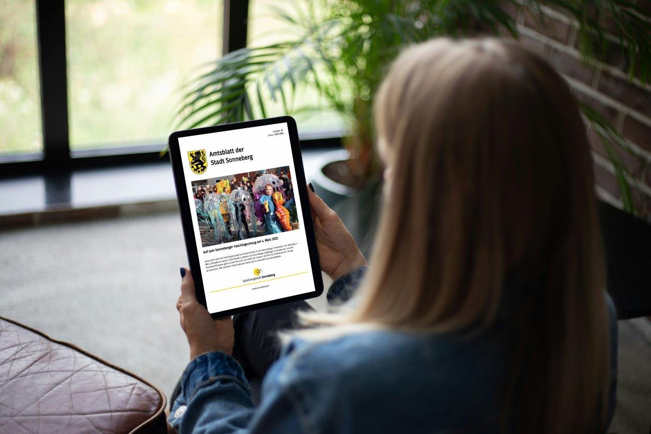 Eine Frau sitzt mit einem Tablet auf der Couch.