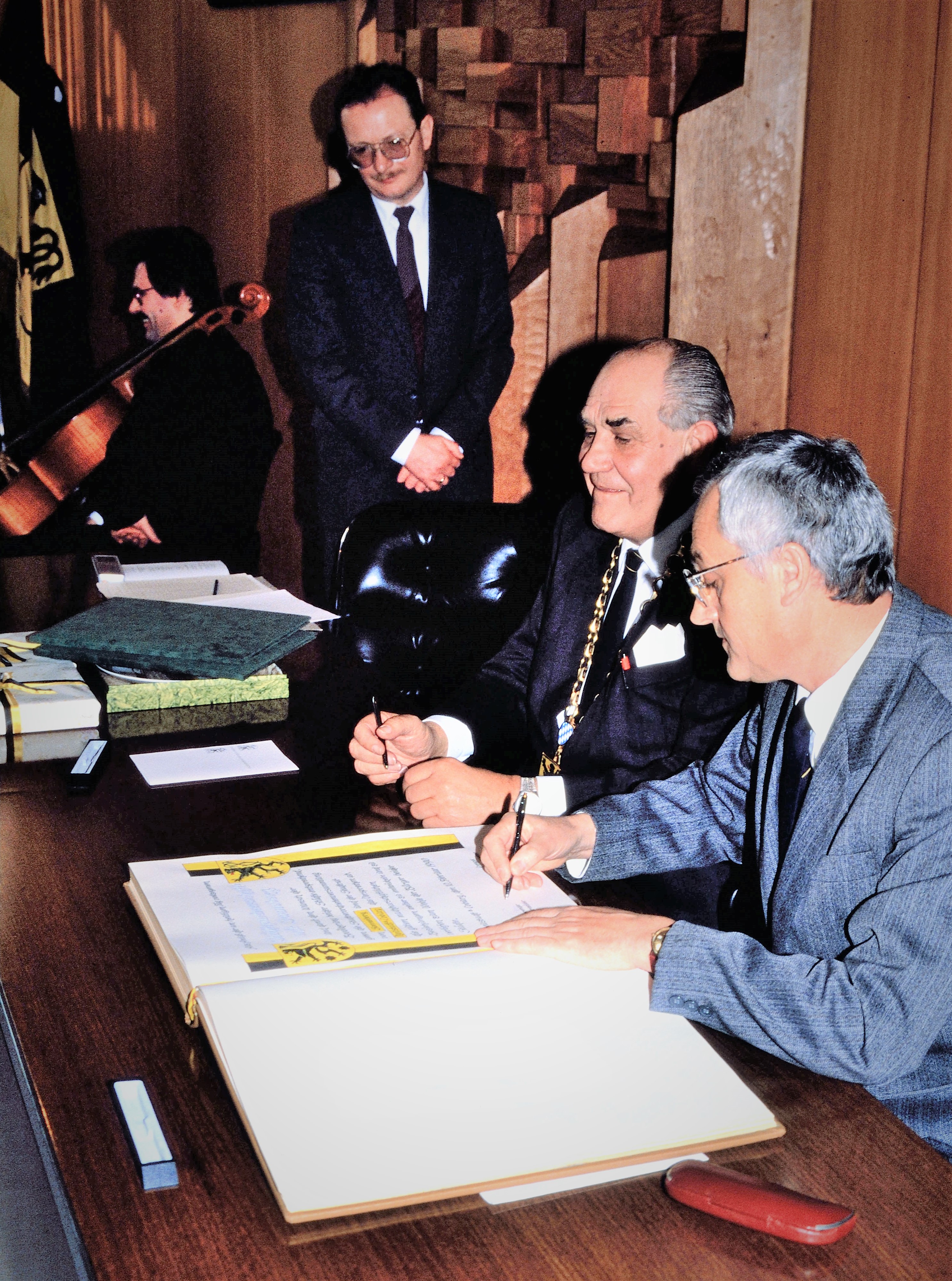 Zwei Männer setzen ihre Unterschrift unter eine Urkunde, die die Städtepartnerschaft besiegeln.