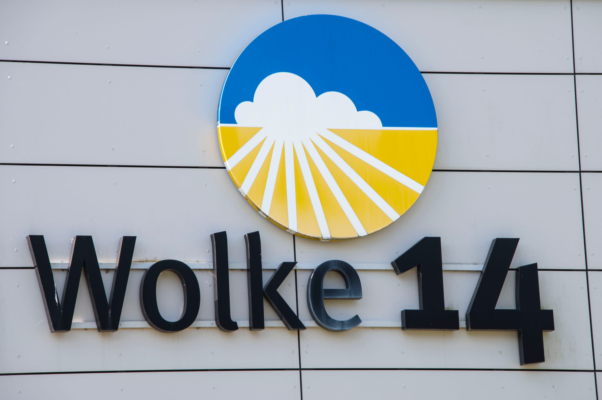 Ein Schild an einer Hauswand. Es trägt die Aufschrift Wolke 14. Darüber ist eine Sonne mit Wolken.