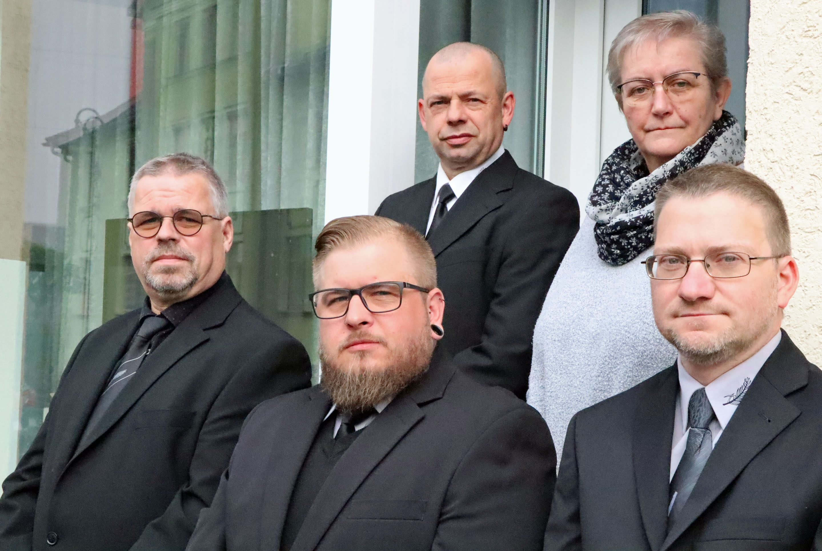 Vier Männer in schwarzen Anzügen und eine Frau stehen vor einer Tür.